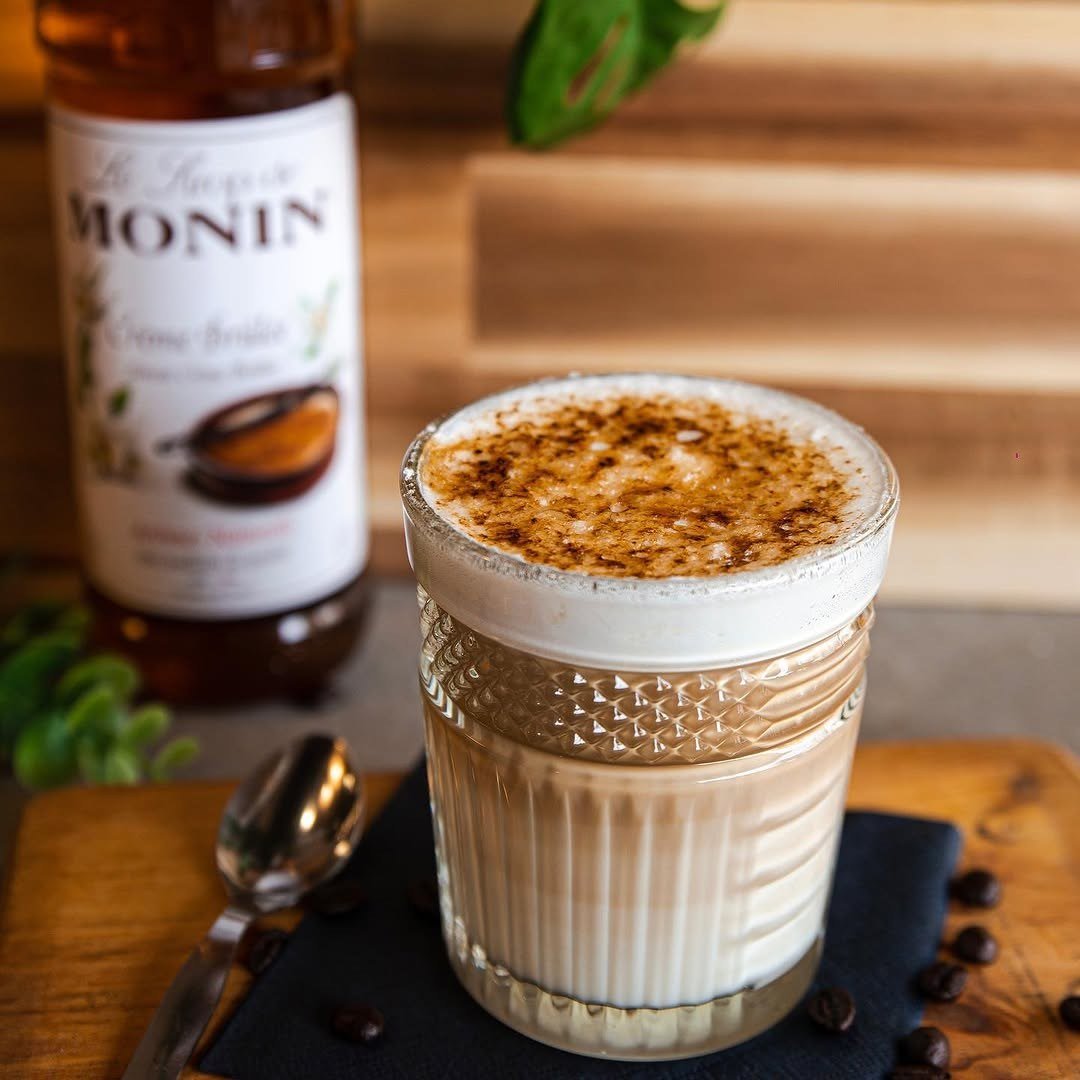 Copo de latte com o topo caramelizado, ao lado de uma garrafa de xarope